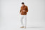 Model wearing brown merino-cashmere blend turtleneck jumper with white trousers, front view.