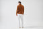 Model wearing brown merino-cashmere blend turtleneck jumper with white trousers, back view.