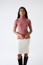 Model wearing a pink turtleneck jumper and white skirt on a white background