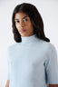 Close-up of model wearing light blue merino wool short-sleeve turtleneck jumper.