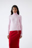 Model wearing pink merino wool turtleneck jumper with red skirt, front view.