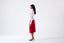 Model wearing pink merino wool turtleneck jumper with red skirt, side view.