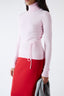 Model wearing pink merino wool turtleneck jumper with red skirt, side view.