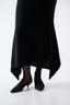 Black dress with a draped design worn by a person on a white background